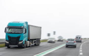 Modern turquoise truck with trailer moving along a wet highway in rainy weather. Motion blur enhances the sense of speed and cargo transportation dynamics.